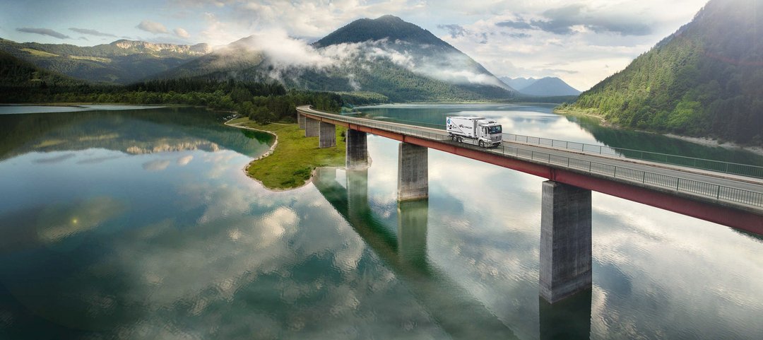 Mercedes-Benz eActros drives over a bridge over a lake in the mountains